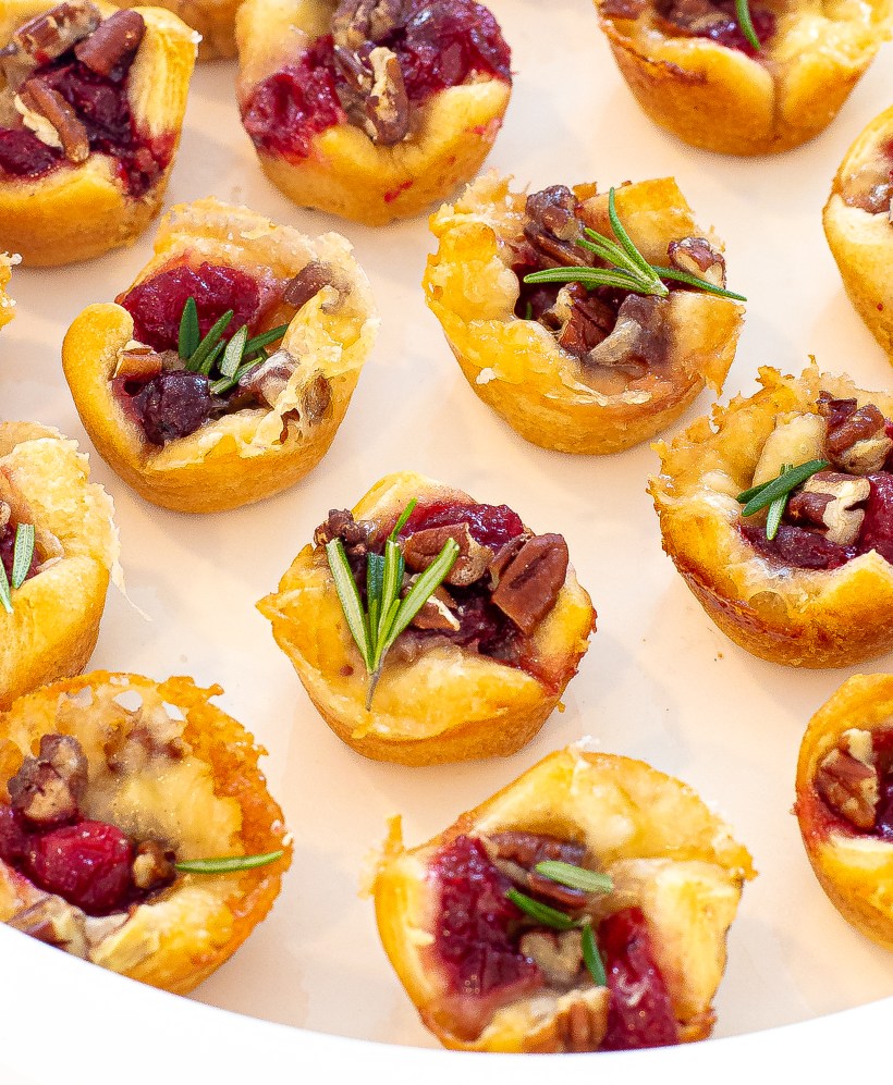 Cranberry brie pastry cups lined up on a white serving plate.